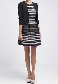 Svart kort kavaj över en randig klänning i varierande nyanser av svart, grått och rosa. Klänningen har en åtsittande överdel och en utfläkt kjol.