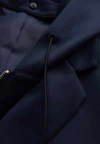 Tissu bleu marine foncé avec un cordon noir passé à travers un œillet en métal et une fermeture éclair partiellement visible sur le côté.