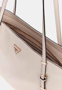 Borsa tote in pelle beige chiaro con due manici, con logo in tonalità oro e una tasca interna con zip. Texture liscia con accenti neri.
