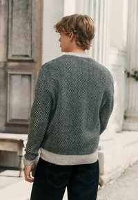 Houndstooth patterned sweater in gray and black with a cream ribbed hem. Knit texture with long sleeves, paired with dark jeans.