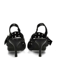 Sandali neri con tacco alto e cinturini alla caviglia, occhielli argentati e fibbie regolabili, mostrati da dietro su sfondo bianco.