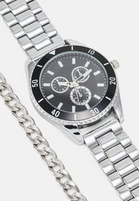 Montre en acier inoxydable argenté avec un cadran noir. Ses caractéristiques incluent trois sous-cadrans, des accents argentés et un bracelet à maillons.