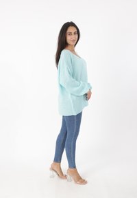 Jasnoniebieski, oversize sweter z teksturowanym splotem, zestawiony z dopasowanymi ciemnoniebieskimi dżinsami i przezroczystymi sandałami na słupku.