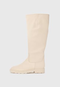 Knee-high krémové kožené čižmy s hladkou text�úrou, zaoblenou špičkou, jemným šitím a nízkym blokovým podpätkom pre väčšiu podporu.