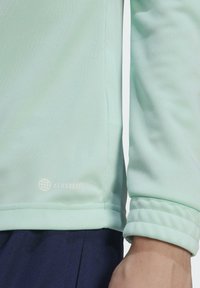 Mintgrünes langärmeliges Sportoberteil mit strukturierter Oberfläche, gerippten Bündchen und einem weißen "AEROREADY" Logo nahe dem Saum.