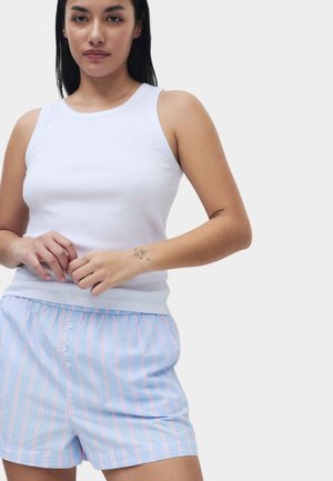 Débardeur blanc côtelé associé à un short de nuit bleu clair à rayures avec des rayures rouges verticales et une patte de boutonnage.