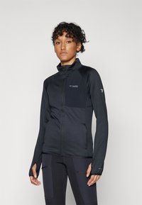 Black zip-up jacket with a textured finish, featuring a stand collar, long sleeves, and a small chest pocket. Accompanied by dark leggings.