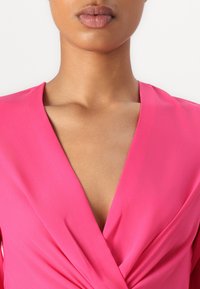 Pink wrap dress with a deep V-neckline, made of smooth fabric. Features subtle draping and cross-over detail at the front.