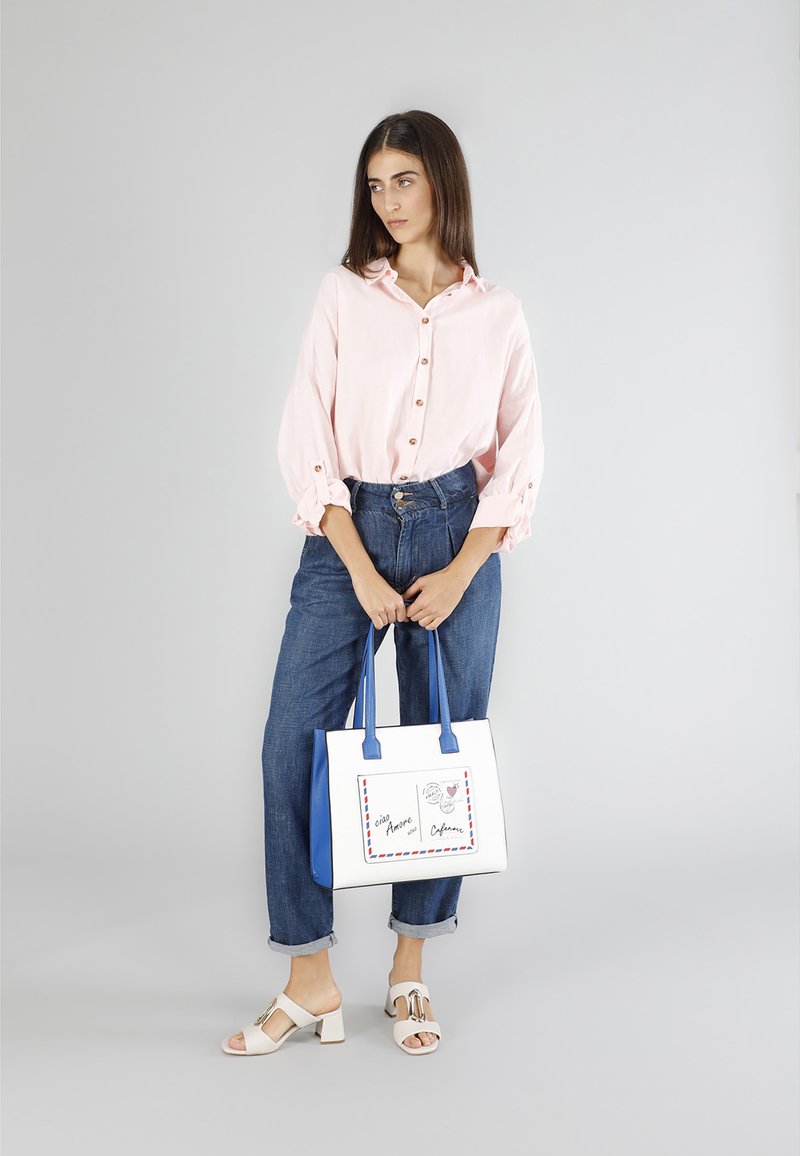 Ljusrosa skjorta med knappar och upprullade ärmar, tillsammans med högmidjade blå denimbyxor och vita klacksandaler med blockklack. Innehåller en vit tote-väska med blå detaljer.