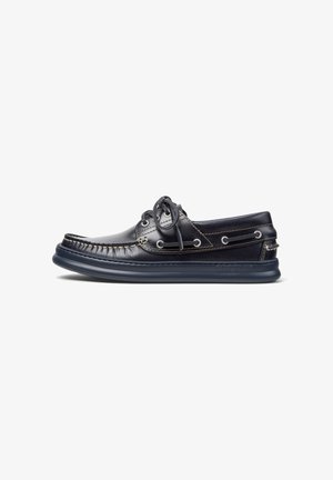 Marine leren bootshoe met decoratieve stiksels en veters, voorzien van een flexibele rubberen zool voor comfort. Zijaanzicht tegen een witte achtergrond.