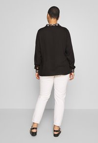 Camicia nera a maniche lunghe con colletto floreale, abbinata a pantaloni bianchi e sandali neri. La camicia ha una vestibilità comoda e un tessuto testurizzato.