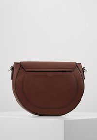 Brązowa skórzana torebka o zaokrąglonym kształcie, z klapką zapinaną na zatrzask oraz subtelnymi przeszyciami. Gładka faktura, minimalistyczne elementy metalowe.