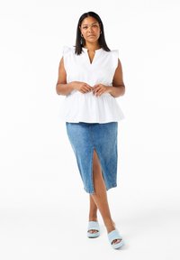 Top bianco a peplum con maniche a volant, gonna a tubino in denim con spacco anteriore e scarpe aperte azzurro chiaro. Sfondo bianco semplice.