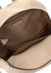 Beige stoffen rugzak interieur met een gladde textuur, ritssluiting en één vak. Heeft een klein label dat in de voering is genaaid.