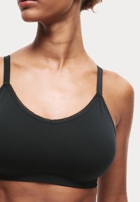 Svart bralette i mjukt tyg, med justerbara axelband, en scalloped kant längs halsringningen och en sömlös design.