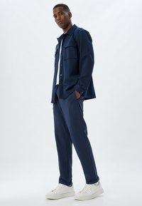 Marine outfit med en skjorte med knapper og to frontlommer, parret med matchende bukser og hvide sneakers. Glat stofstruktur.