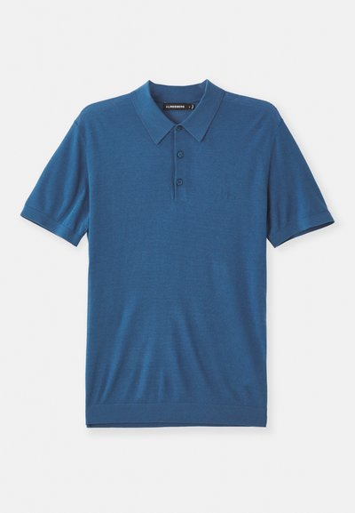 Sinine polo särk pehmest kangast, millel on krae, kolmest nööbist koosnev nööpide rida ja lühikesed varrukad. Rinnaosale on lisatud diskreetne logo detail.