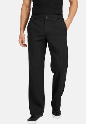 Zwarte op maat gemaakte broeken met een recht model, platte voorkant en elastische tailleband, gedragen met een zwart shirt en casual schoenen.