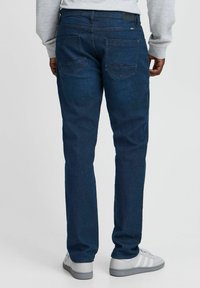 Vaqueros de denim azul con corte recto, que presentan dos bolsillos traseros y una textura sutil. Combinados con zapatillas grises.