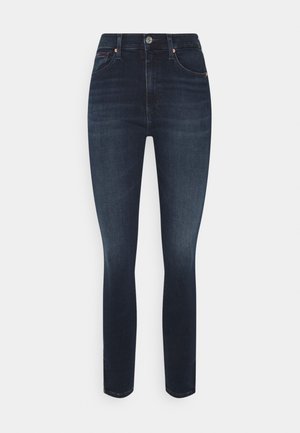 Jeans skinny de talle alto en azul oscuro, con bolsillos frontales, cierre de botón y un ligero desgaste en los muslos y las rodillas.