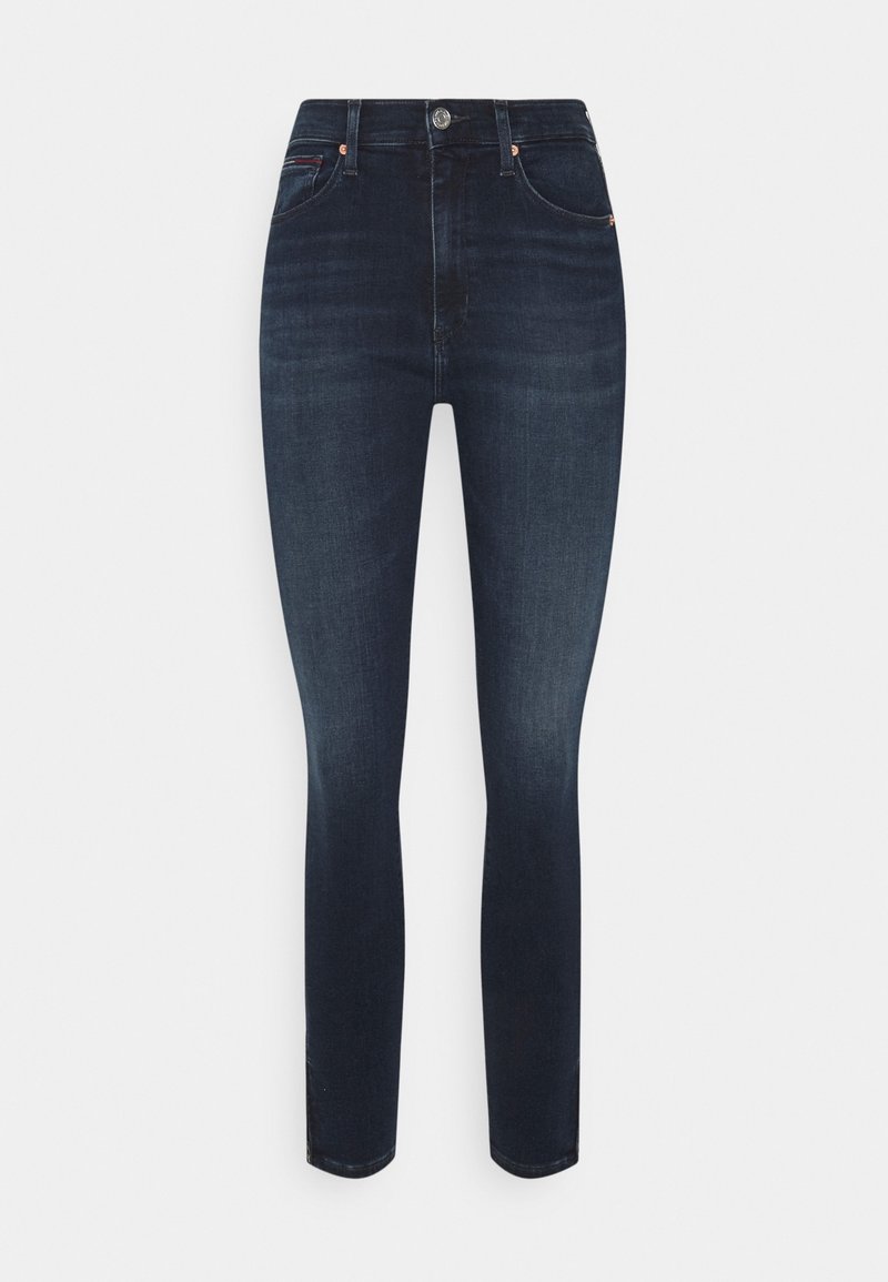 Jeans skinny de talle alto en azul oscuro, con bolsillos frontales, cierre de botón y un ligero desgaste en los muslos y las rodillas.
