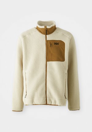 Veste en polaire crème avec une poche poitrine marron. Dotée d'un col montant, de fermetures éclair et d'un tissu texturé pour l'isolation.