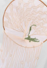 Gesticktes Design mit einem Baum in beige Umriss und grünen Akzenten, auf weißem Hintergrund gesetzt. Enthält perlenartige Details darunter.