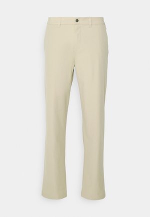Beżowe spodnie o prostym kroju nogawki, z przodem na guzik i szlufkami na pasek. Gładka faktura tkaniny, bez widocznych wzorów.