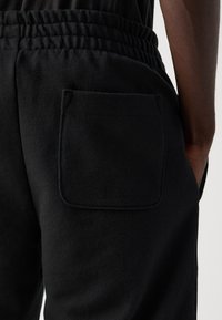 Nærbilde av en person som har på seg svarte joggebukser med elastisk liv og en firkantet baklomme.
