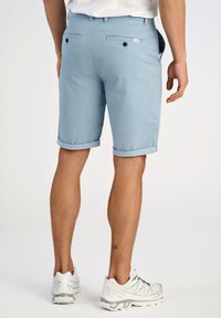 Ljusblå mönstrade shorts i ett texturerat tyg. Har vikta fållar, två bakfickor med knappar och bältesöglor. Bärs med vita sneakers.