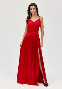 Červené saténové večerní �šaty s obálkovým designem, tenkými ramínky a vysokým rozparkem. Mají hladkou texturu a délku až na podlahu.
