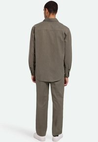 Oliven grøn skjorte med knaplukning og lange ærmer, bagryg detaljer, og en afslappet pasform, parret med matchende tapered bukser og hvide sneakers.