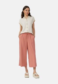 Lichtbeige short-sleeve shirt met knopen, gecombineerd met lichtroze wijde broek met een elastische tailleband. Gekocht met crèmekleurige platform sandalen.
