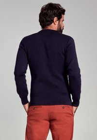 Pull en tricot bleu marine avec un col rond et des poignets côtelés, porté avec un pantalon orange. Le tissu semble doux avec une texture lisse.