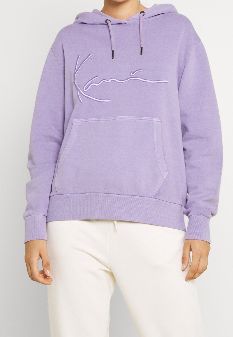 Lila hoodie med kängurufickor, med broderad text på framsidan. Mjuk, texturerad tyg; ribbad ärm och nederkant.