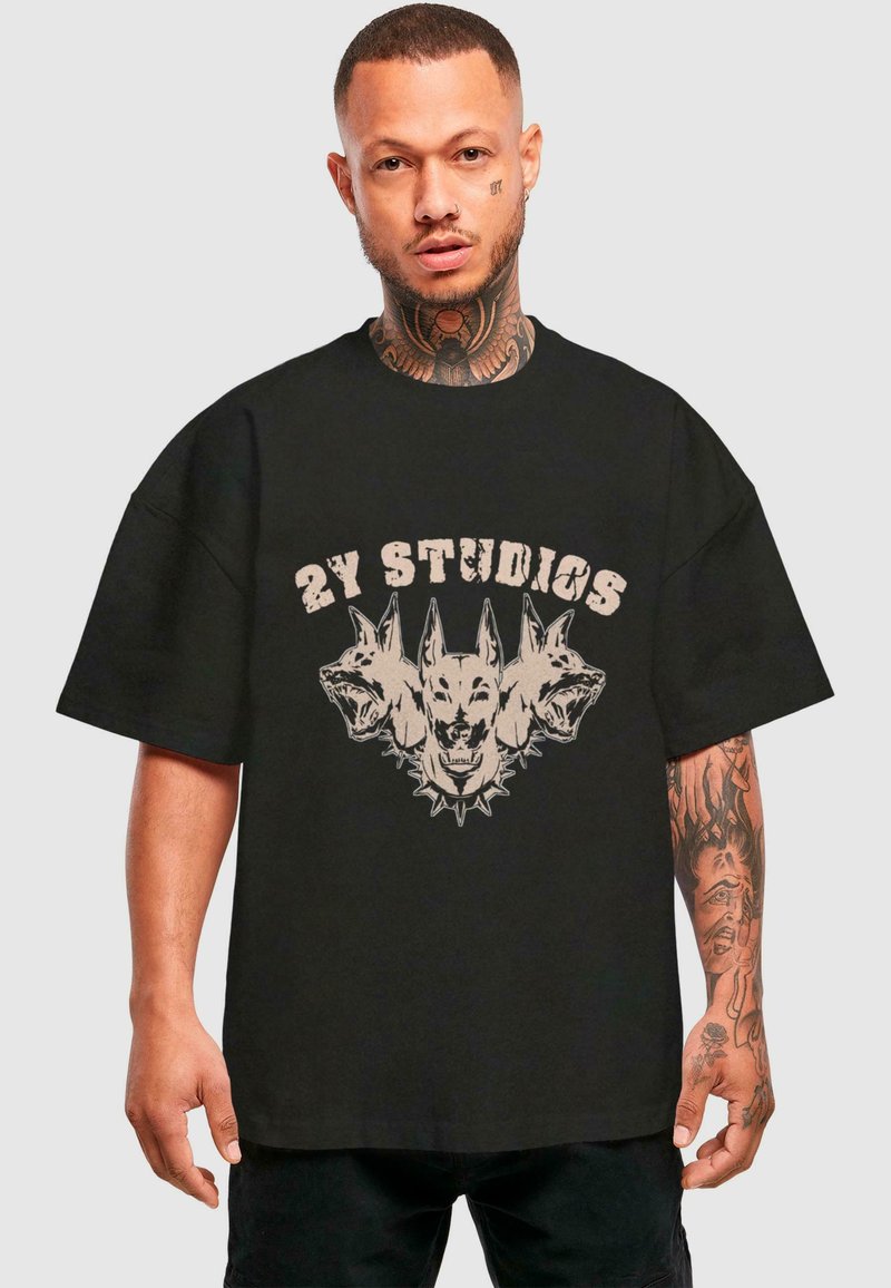 Černé oversized tričko s grafickým designem tří psích hlav a nápisem "2Y STUDIOS" v opotřebovaném béžovém písmu. Krátké rukávy, volný střih.