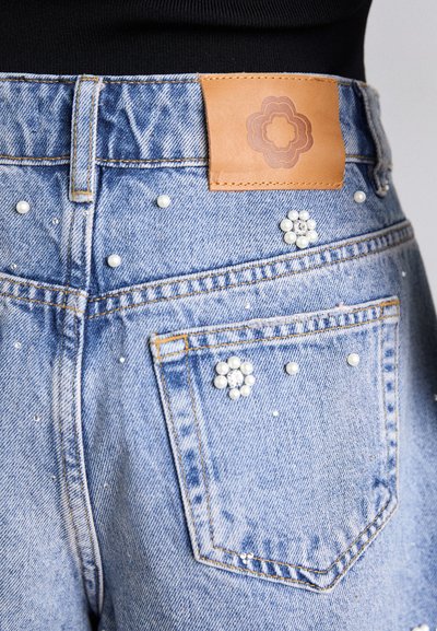 I pantaloni shorts di jeans blu chiaro presentano un'etichetta in pelle marrone, perle decorative e decorazioni floreali sulle tasche posteriori.