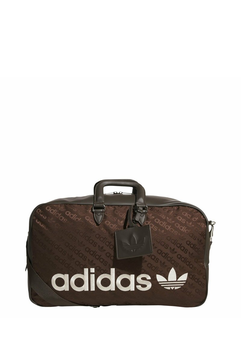 Brown duffel bag with a smooth texture, featuring a large white "adidas" logo and a subtle branded pattern. Includes dual handles and a tag.