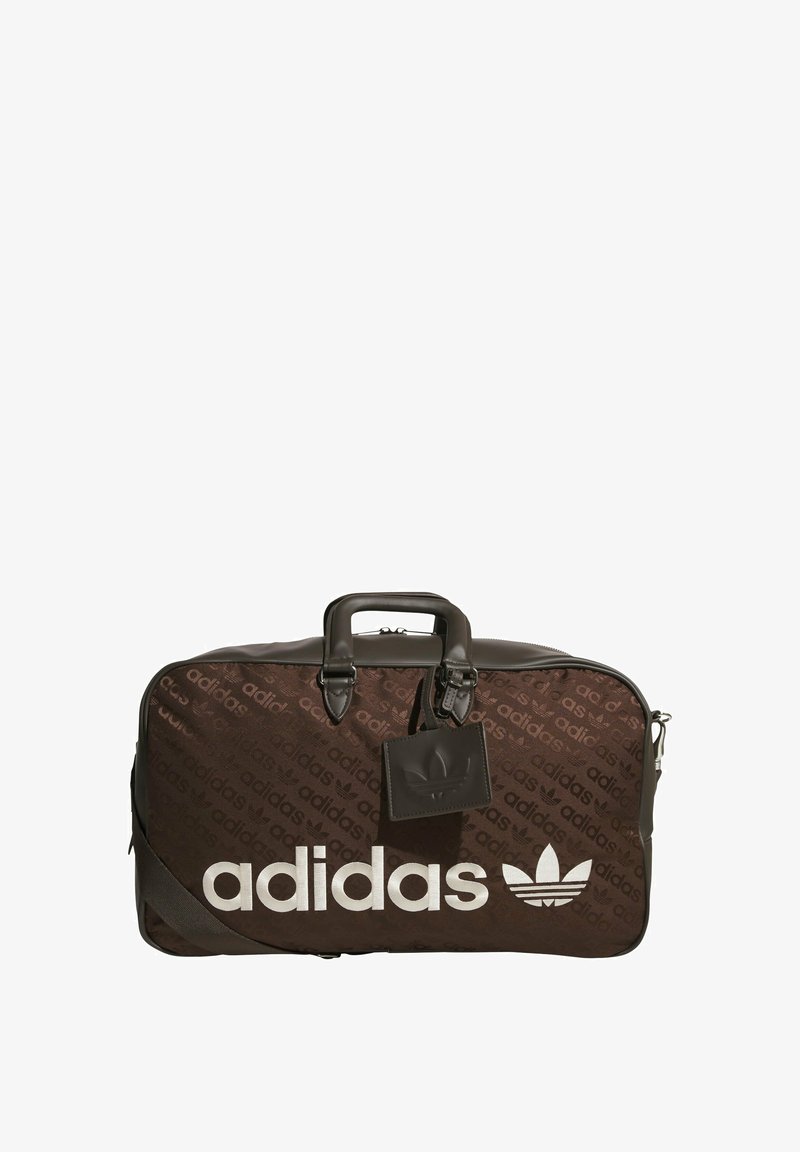 Bruine sporttas met een gladde textuur, voorzien van een groot wit "adidas"-logo en een subtiel merpatroon. Is uitgerust met dubbele handvatten en een label.