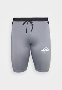 Shorts de sport gris en tissu stretch. Présentent une taille noire avec cordon de serrage et un logo Nike Trail blanc sur le côté.