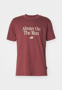 Maroon T-shirt met korte mouwen met daarop de tekst "Altijd Op De Ren" en het New Balance-logo in het wit afgedrukt aan de voorkant.