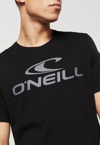 Sort bomulds t-shirt med et stort gråt O'Neill-logo tværs over brystet. Rund halsudskæring og korte ærmer. Glat tekstur.