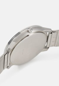 Montre en acier inoxydable avec un boîtier rond, un bracelet en maille et une couronne proéminente. Présente une surface lisse et réfléchissante avec un design minimaliste.