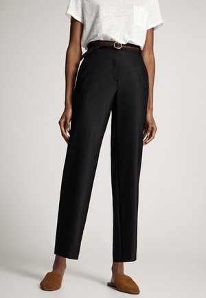 Person iført sorte, højttaljede bukser med lige ben, et brunt flettet bælte, en hvid kortærmet skjorte og brune slip-on sko.