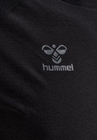Zwarte stof met een reflecterend zilveren hummel-logo met een gestileerde hommel boven de merknaam.