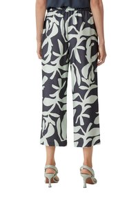 Culotte-broeken met een zwart en mintgroen bladerenpatroon, elastische tailleband en rechte snit. Draagbaar met lichtgroene hoge hakken.