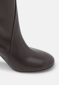 Svart läderankelboots med spetsig tå, slankt design och en mjuk textur. Har en avsmalnande klack för stabilitet.