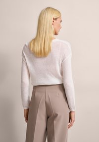 Helles pinkfarbiges, weich gestricktes Sweatshirt mit langen Ärmeln und rundem Ausschnitt, kombiniert mit hoch taillierten beigen Hosen mit Falten.