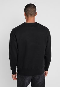 Felpa nera a girocollo con maniche lunghe, polsini e orlo a costine, realizzata in un materiale morbido e texture. Design semplice e non decorato.