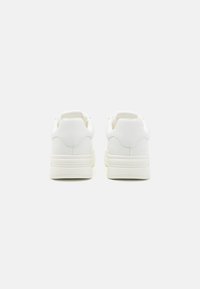 Hvite sneakers med glatt syntetisk materiale, rund tå, polstret krage og solid gummisåle. Minimalistisk design uten synlige logoer.